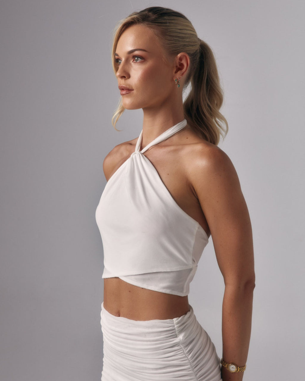 Side view of Elara ivory halter crop top with twisted neckline detail styled with the Elara sheer maxi skirt in studio.