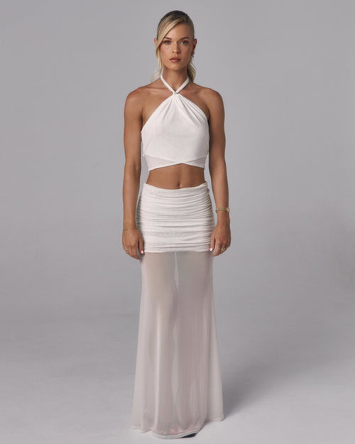 Model wearing Elara ivory sheer maxi skirt with ruched mini lining and white halter top in a studio setting.