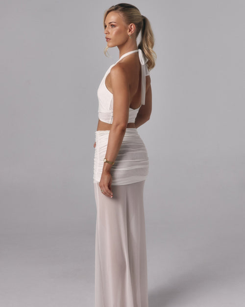 Side view of Elara ivory sheer maxi skirt with ruched mini lining styled with a white halter top in a studio setting.
