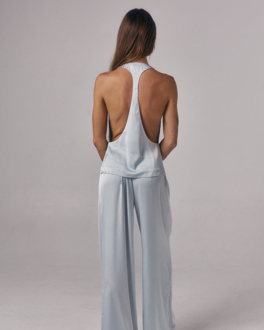 Back view of Paloma light blue satin lounge pants styled with matching satin racerback top in a studio setting.
