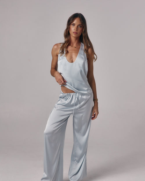 Model wearing Paloma light blue satin lounge pants with drawstring waist and wide leg fit in a studio setting.