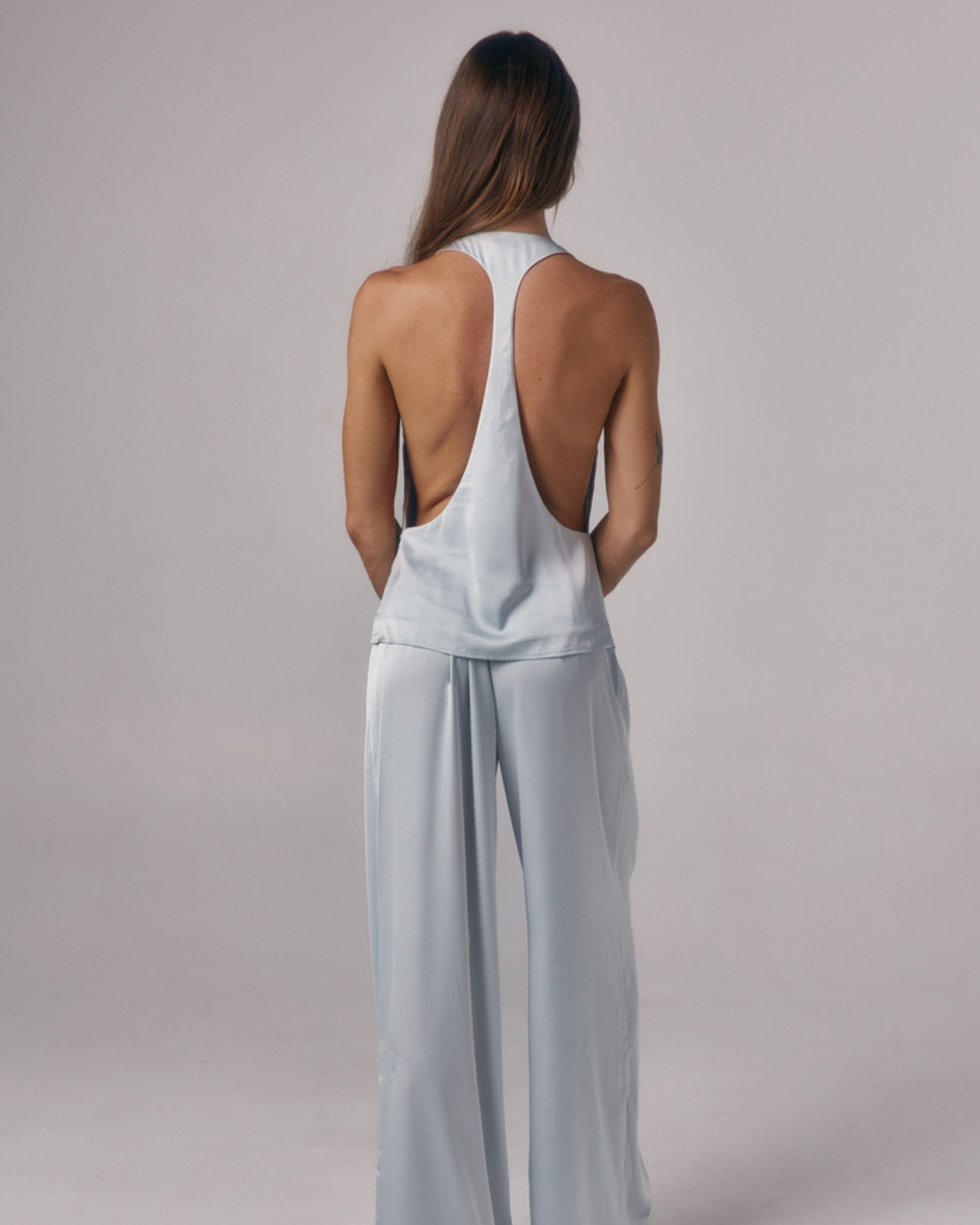 Back view of Paloma light blue satin halter top with open racerback detail styled with matching satin lounge pants in studio.