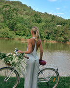 Back view of Paloma light blue satin halter top styled with matching satin lounge pants by a lake with a bicycle.