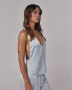 Side view of Paloma light blue satin halter top with deep neckline styled with matching satin lounge pants in studio.