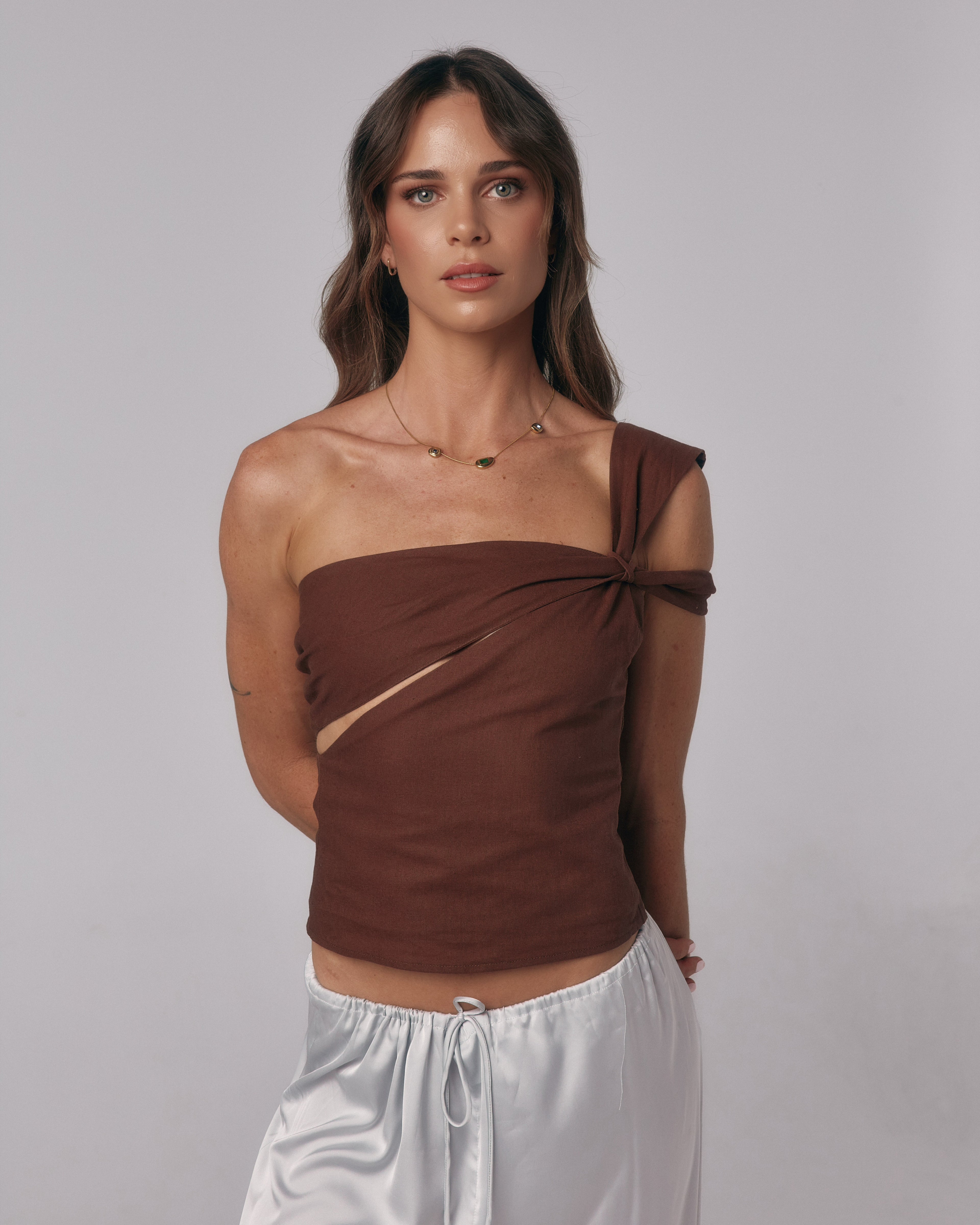 Close-up front view of model wearing the Sienna Top in espresso, an asymmetric one-shoulder fitted top with twist detail.