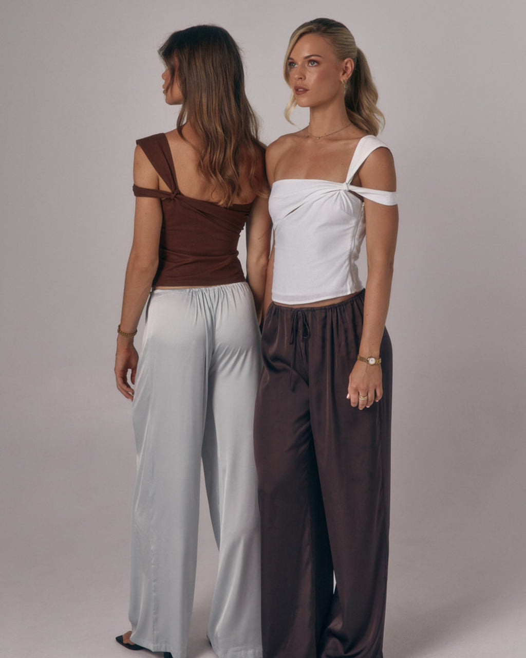Two models wearing the Sienna Top in ivory and espresso showing front and back views of the asymmetric one-shoulder design.