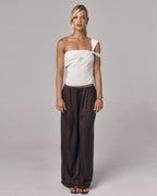 Front view of model wearing the Sienna Top in ivory, an asymmetric one-shoulder fitted top styled with relaxed brown pants in studio.