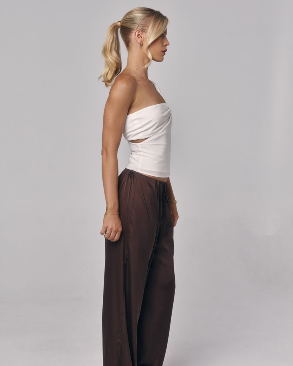 Side view of model wearing the Sienna Top in ivory, a strapless fitted top styled with relaxed brown pants in a studio setting.