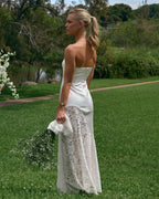 Back view of Soleil ivory strapless maxi dress with lace skirt panel outdoors by a lake and greenery.