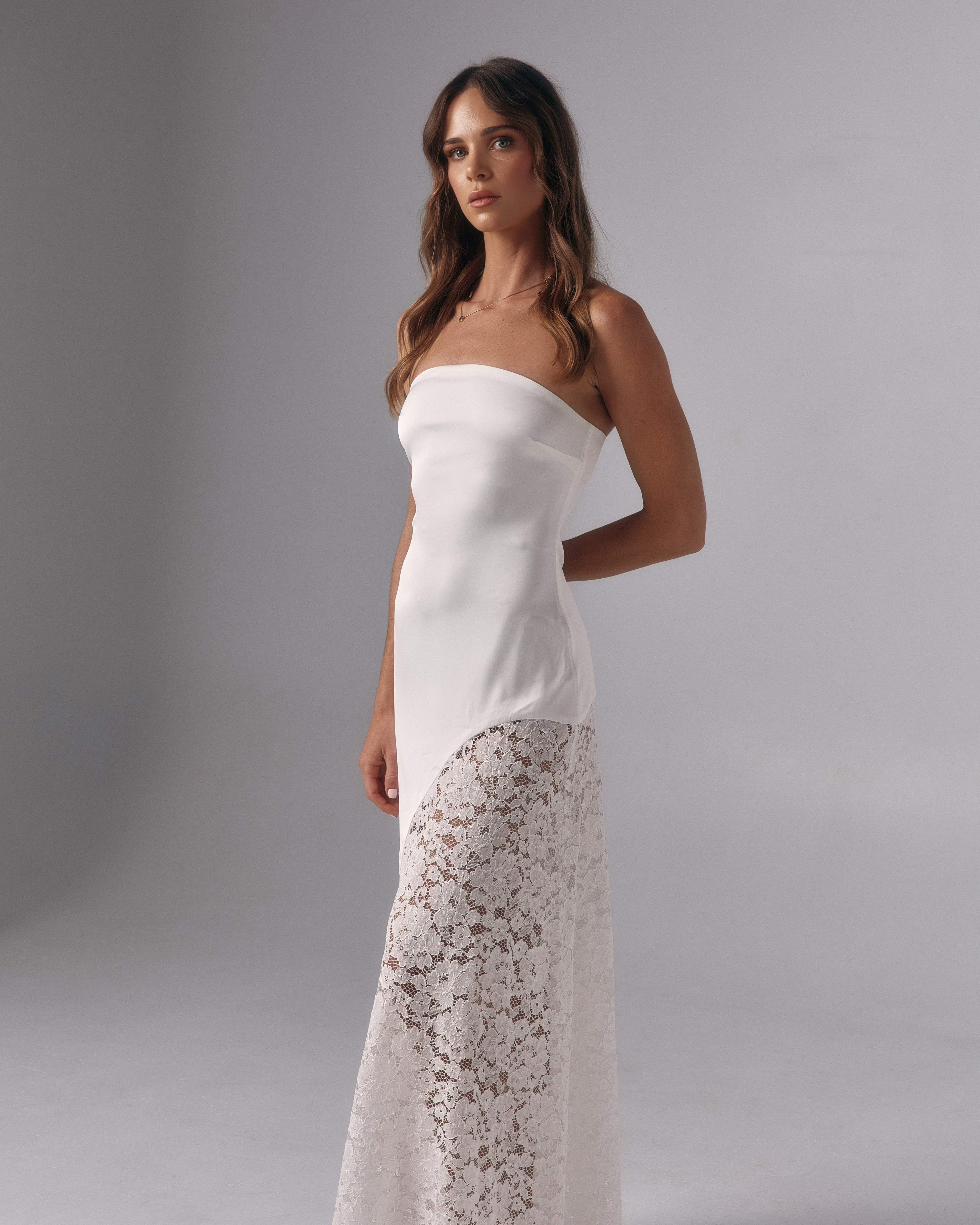 Model wearing Soleil ivory strapless maxi dress with lace skirt panel in a studio setting