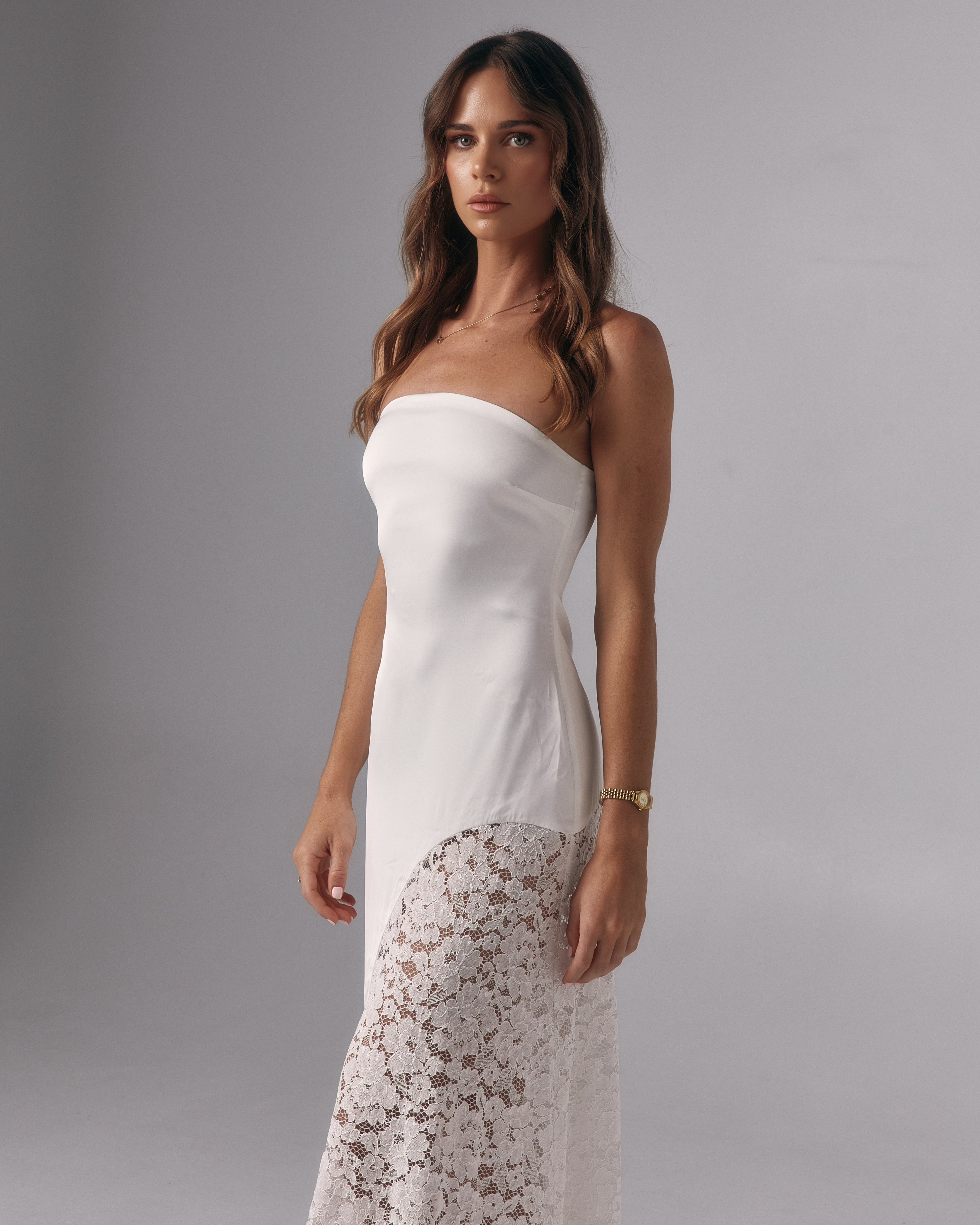Model wearing Soleil ivory strapless maxi dress with fitted bodice and curved lace skirt panel in studio.
