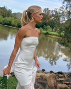 Model wearing Soleil ivory strapless maxi dress with lace skirt panel outdoors beside a lake.