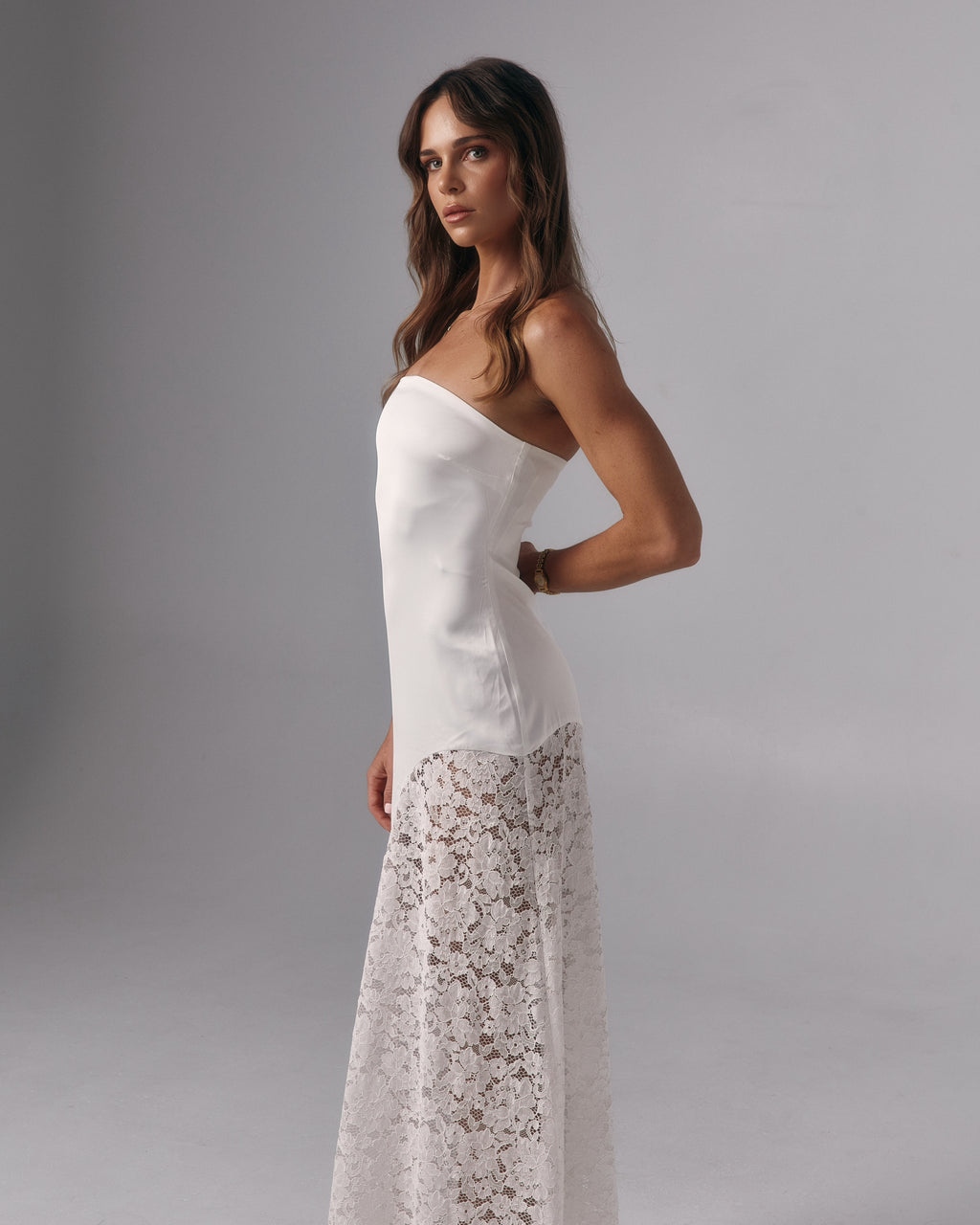 Side profile of Soleil ivory strapless maxi dress with fitted bodice and lace maxi skirt in a studio setting.