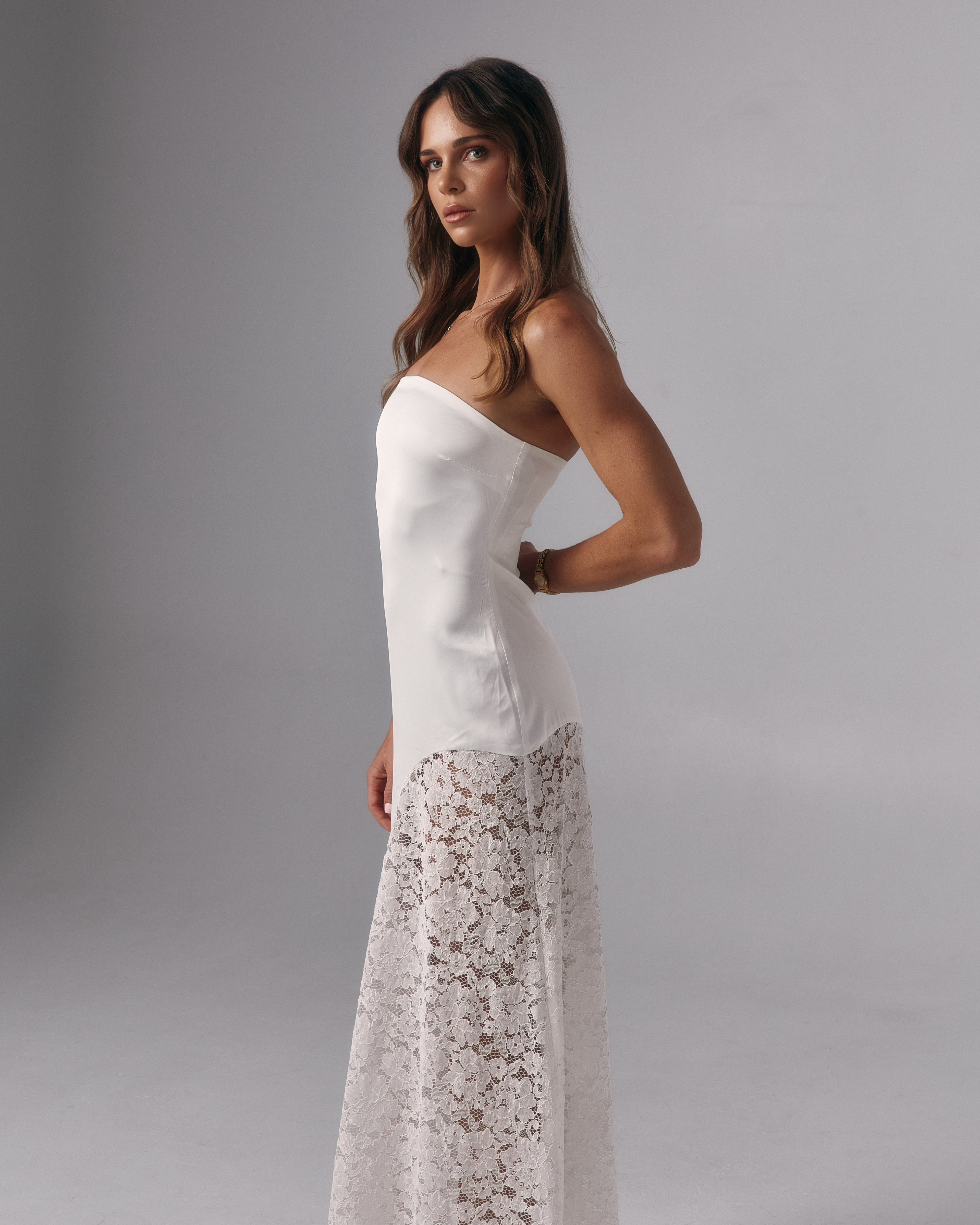 Side profile of Soleil ivory strapless maxi dress with fitted bodice and lace maxi skirt in a studio setting.